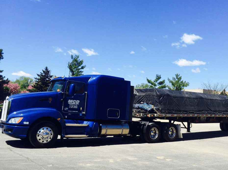 Royal blue MCD Express semi tractor hauling a flatbed trailer loaded with covered freight