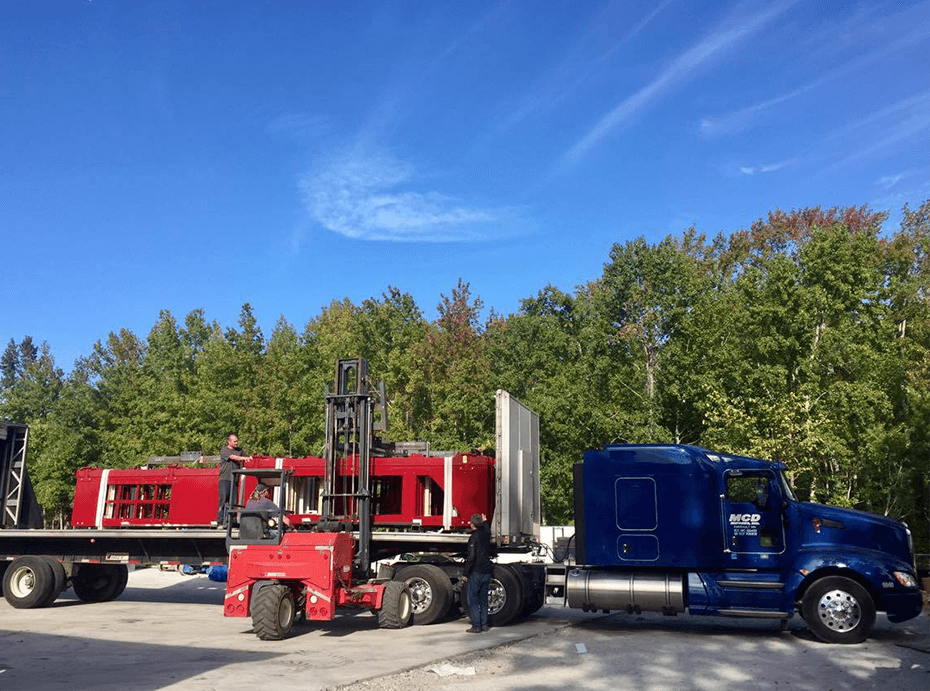 Royal blue MCD Express semi tractor hauling a flatbed trailer getting loaded with metal beams by a forklift