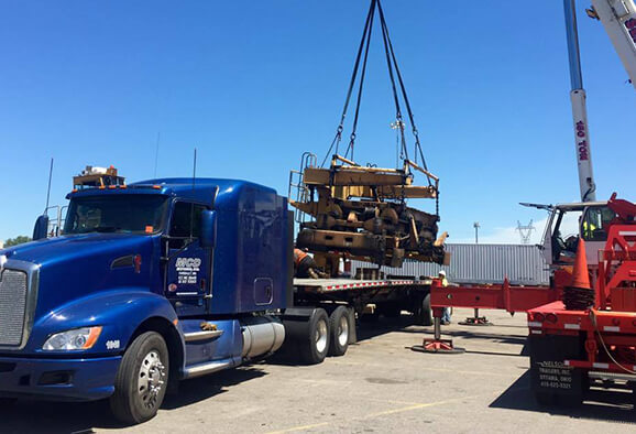 Royal blue MCD Express semi tractor with flatbed trailer getting loaded with an industrial metal structure